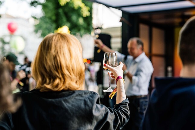Woman standing with her back to the camera at an event and toasting with a glass of prosseco.