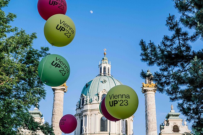 Balloons floating in the air against a blue sky in front of the Vienna Karlskirche.
