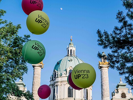 Balloons floating in the air against a blue sky in front of the Vienna Karlskirche.