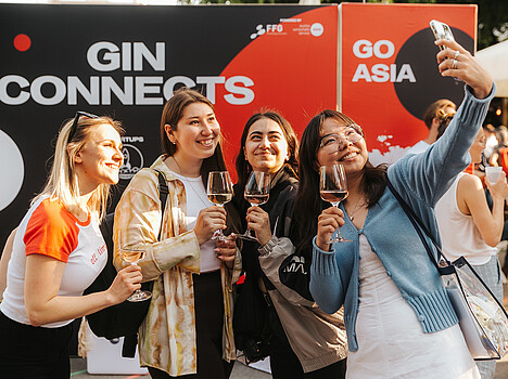 A group of four women enjoying drinks and taking a selfie outdoors at an event.