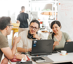 Two men and a woman with computers talking. 