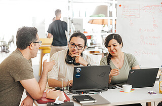 Two men and a woman with computers talking. 