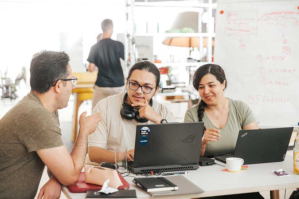 Two men and a women with computers talking. 