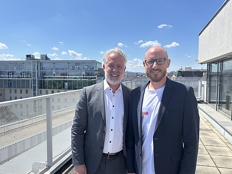 Two men standing on a rooftop terrace