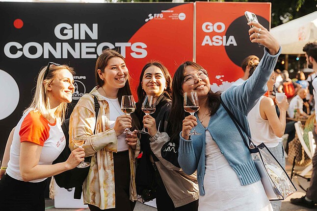 A group of four women enjoying drinks and taking a selfie outdoors at an event.