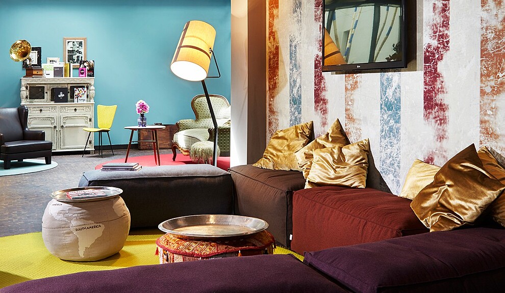 Colorful interior of hotel 25hours, featuring a turquoise wall and comfy sofa with many throw pillows. 