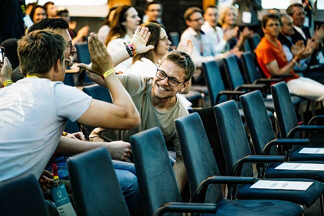 Two men high-fiving while sitting down in the audience of an event.