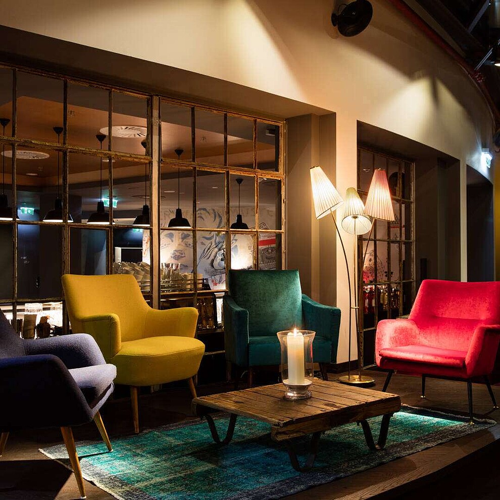 A lounge in the Ruby Marie hotel lobby at night, with warm lighting on four armchairs that are gray, yellow, green and red.