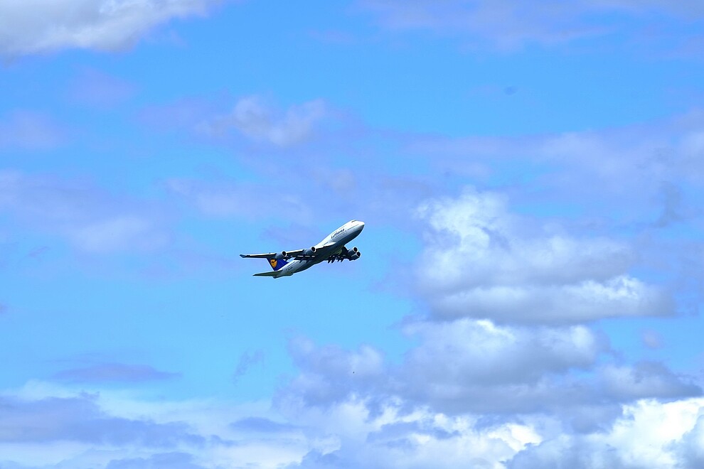 A Lufthansa plane flies across a brilliant blue sky with clouds. 